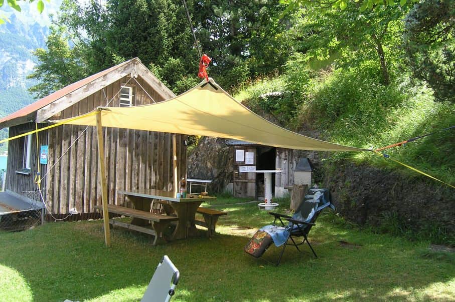 Clubhaus mit Dreieckblache, darunter ein Tisch mit Bank und Liegestühle